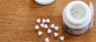 Öppnad burk med läkemedel. Hjärtformade tabletter på en bordsskiva. 