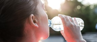 Kvinna som dricker vatten ur en plastflaska en varm sommardag.