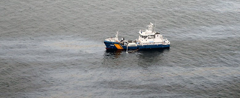 Kustbevakningsfartyg på vatten med oljespill.