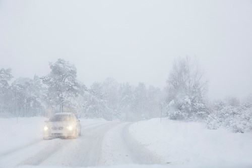 Bil på landsväg under snöstorm.