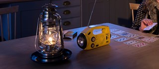 En fotogenlampa står på ett bord bredvid en gul vevradio. Rummet är mörkt. 