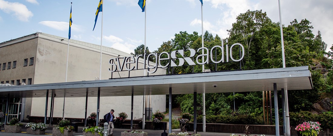 Radiohuset i Stockholm. Fem flaggstänger står utanför byggnaden. I bakgrunden syns träd.