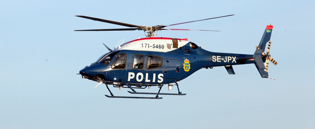 En flygande mörkblå polishelikopter. Blå himmel i bakgrunden.