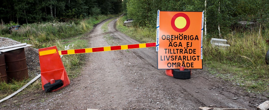 Avspärrad grusväg. På vägen finns en orange skylt med texten "Obehöriga äga ej tillträde. Livsfarligt område".