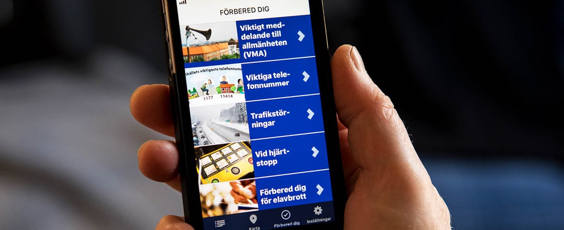 En hand som håller i en smartphone. På skärmen syns information från Krisinformation.se:s app.