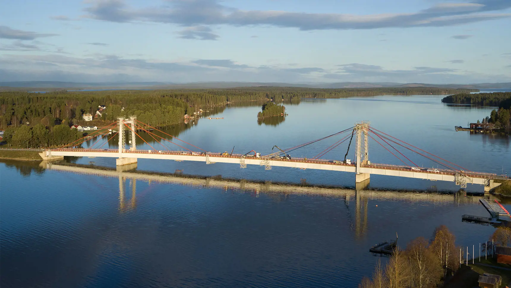 Bild på Strömsundsbron. Skog och hus syns i bakgrunden. Vattnet är stilla.