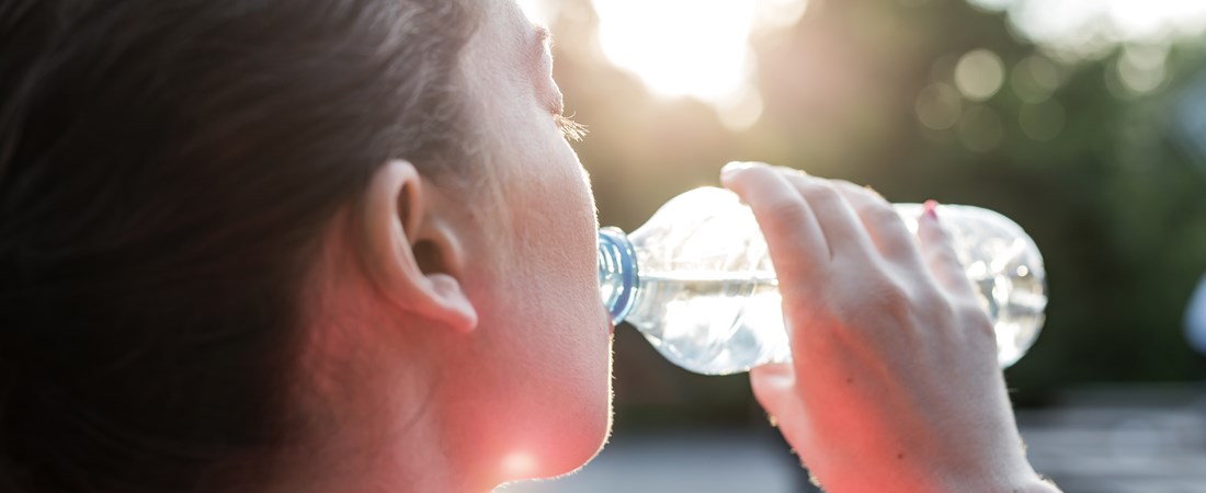 Kvinna som dricker vatten ur en plastflaska en varm sommardag.