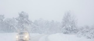 Bil på landsväg under snöstorm.