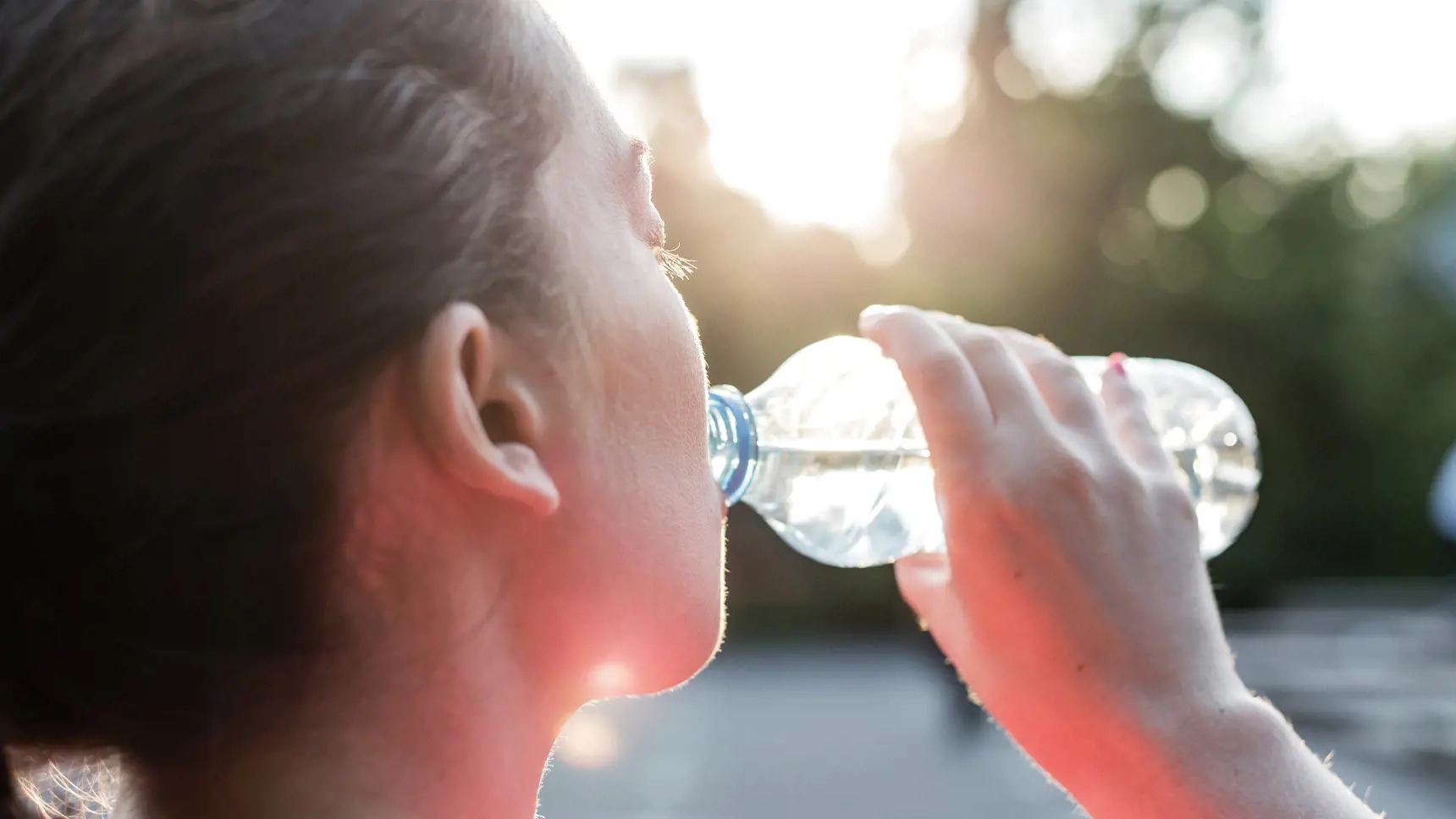 Woman drinking water from a bottle on a sunny day.