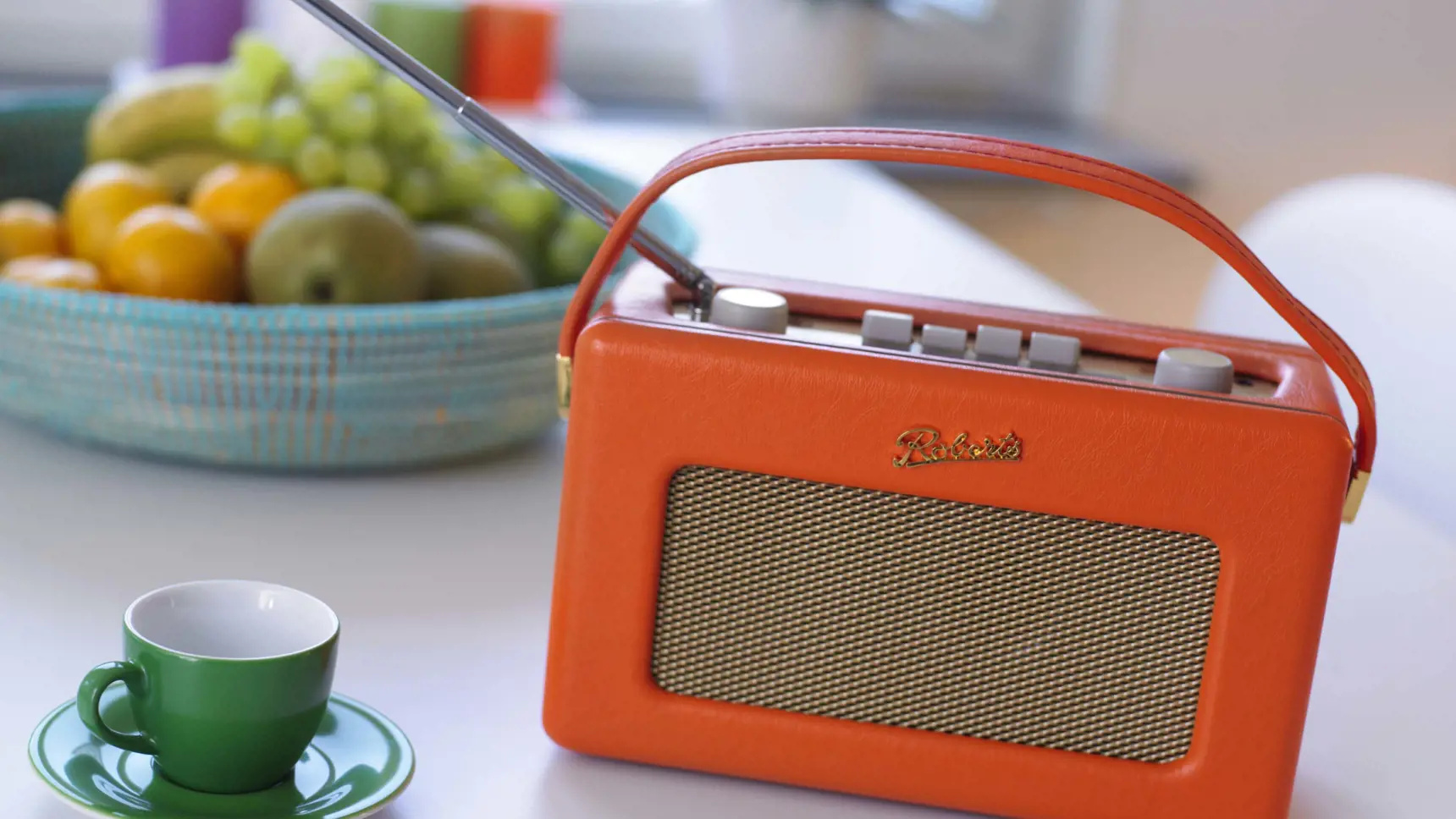 Radioapparat står på köksbord, vid en kaffekopp och en fruktskål.