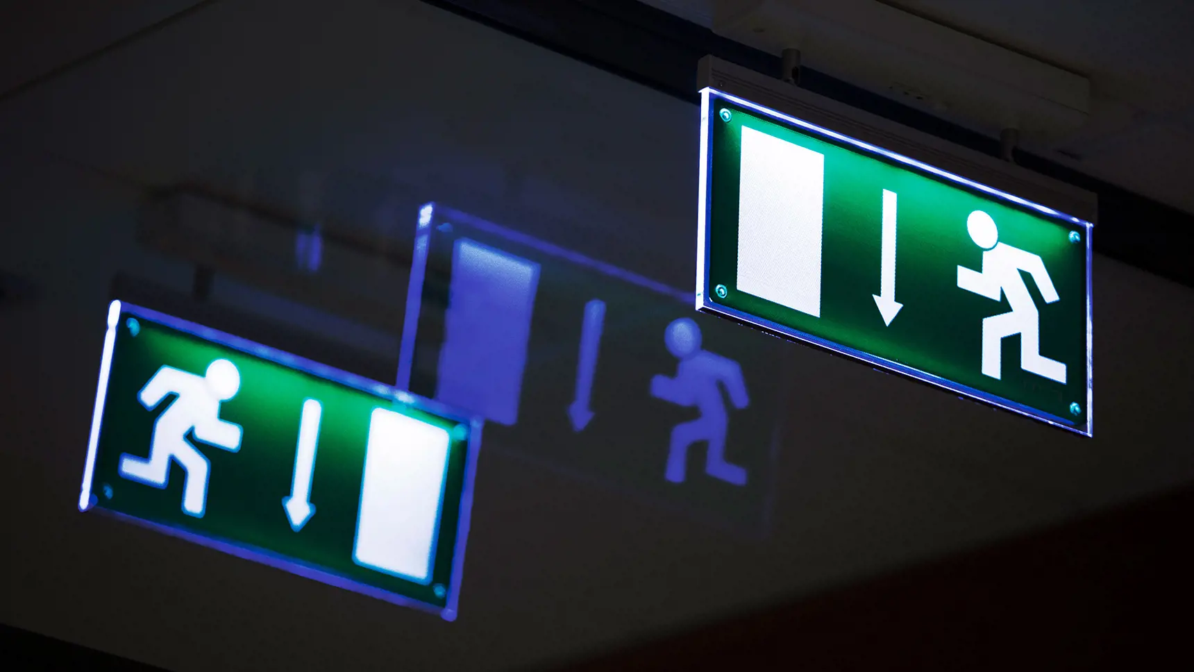Tre gröna skyltar som signalerar nödutgång lyser i mörkret.