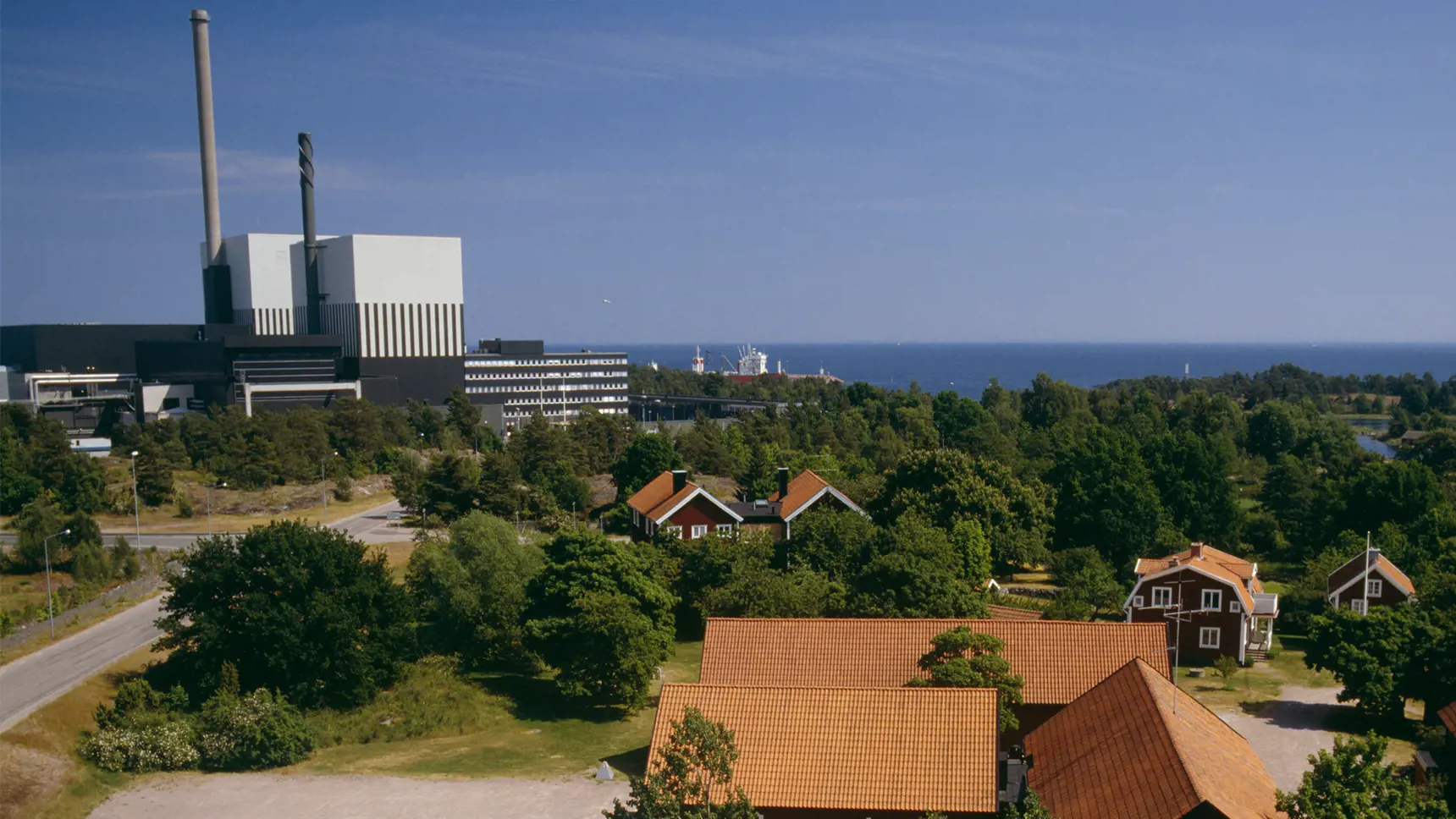 Röd hus och lador med Oskarshamns kärnkraftverk i bakgrunden.
