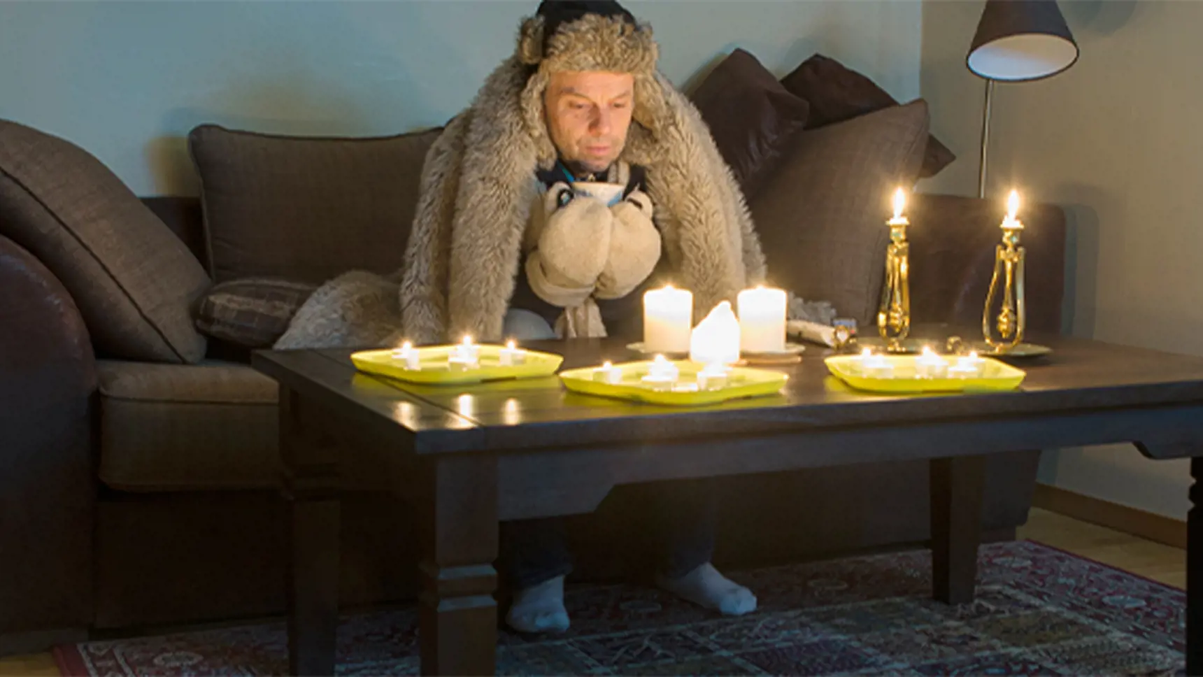 Man sitter och fryser i en soffa med tända stearinljus på bordet.