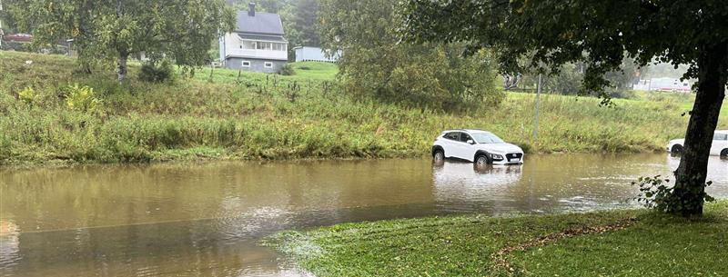 Översvämmat område framför villatomt. Bilar syns i vattnet.