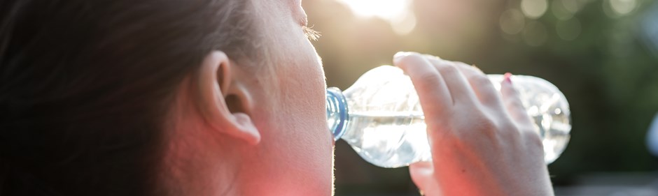 Kvinna som dricker vatten ur en plastflaska en varm sommardag.