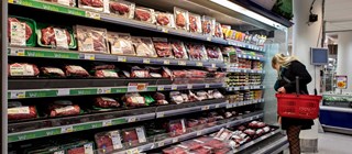 Hylla med köttprodukter i en livsmedelsbutik. Kvinna med korg som handlar.