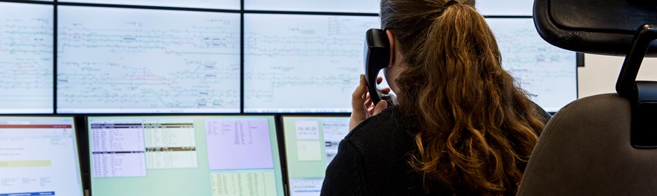 Larmoperatör talar i telefon vid en stor vägg av digitala skärmar.