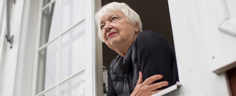 Märta-Lena står med öppet fönster och lutar sig ut över fönsterblecket.