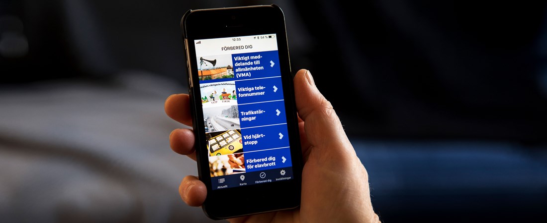 Hand håller i mobiltelefon som har Krisinformation.se:s app på skärmen.