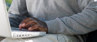Person med grå långärmad tröja skriver på en vit dator.