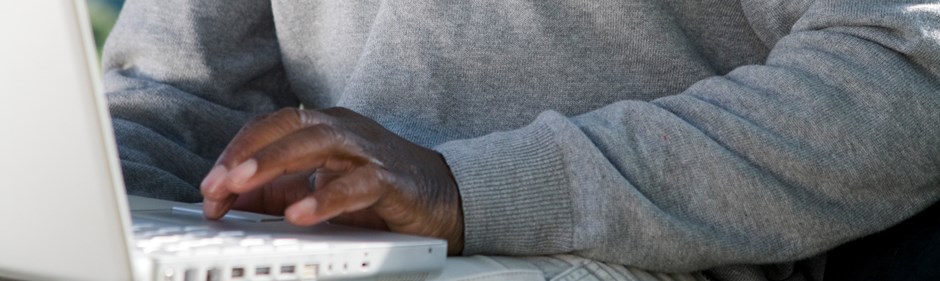 Person med grå långärmad tröja skriver på en vit dator.