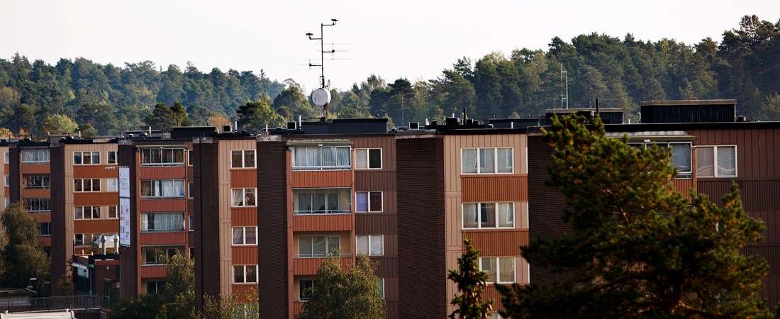 Bruna flerbostadshus med skog i bakgrunden.