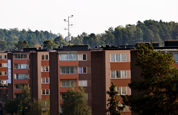 Bruna flerbostadshus med skog i bakgrunden.