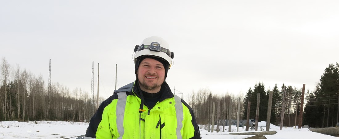 Oscar iförd varselkläder framför kraftledningar. Det är snö på marken.