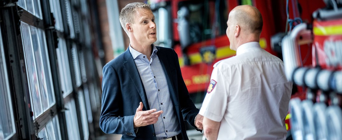 Patrik samtalar med en person framför två röda brandbilar.