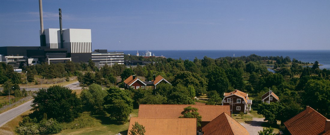 Röda hus i förgrunden. I bakgrunden syns kärnkraftverket Simpevarp i Oskarshamn. Havet är blått och himlen är klarblå.