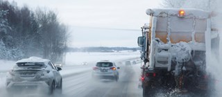 Bilar och plogbil som kör i vinterlandskap på motorväg.