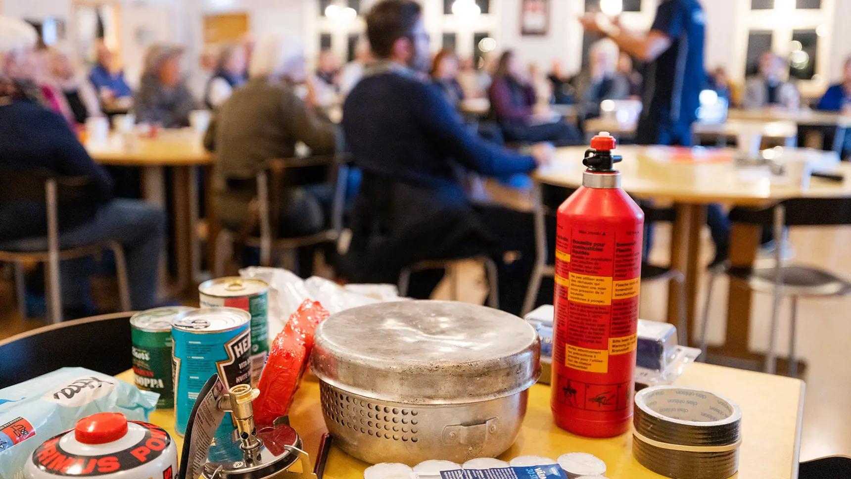 Krisberedskapsutbildning i bakgrunden. Innehåll från en krislåda på ett bord i förgrunden.