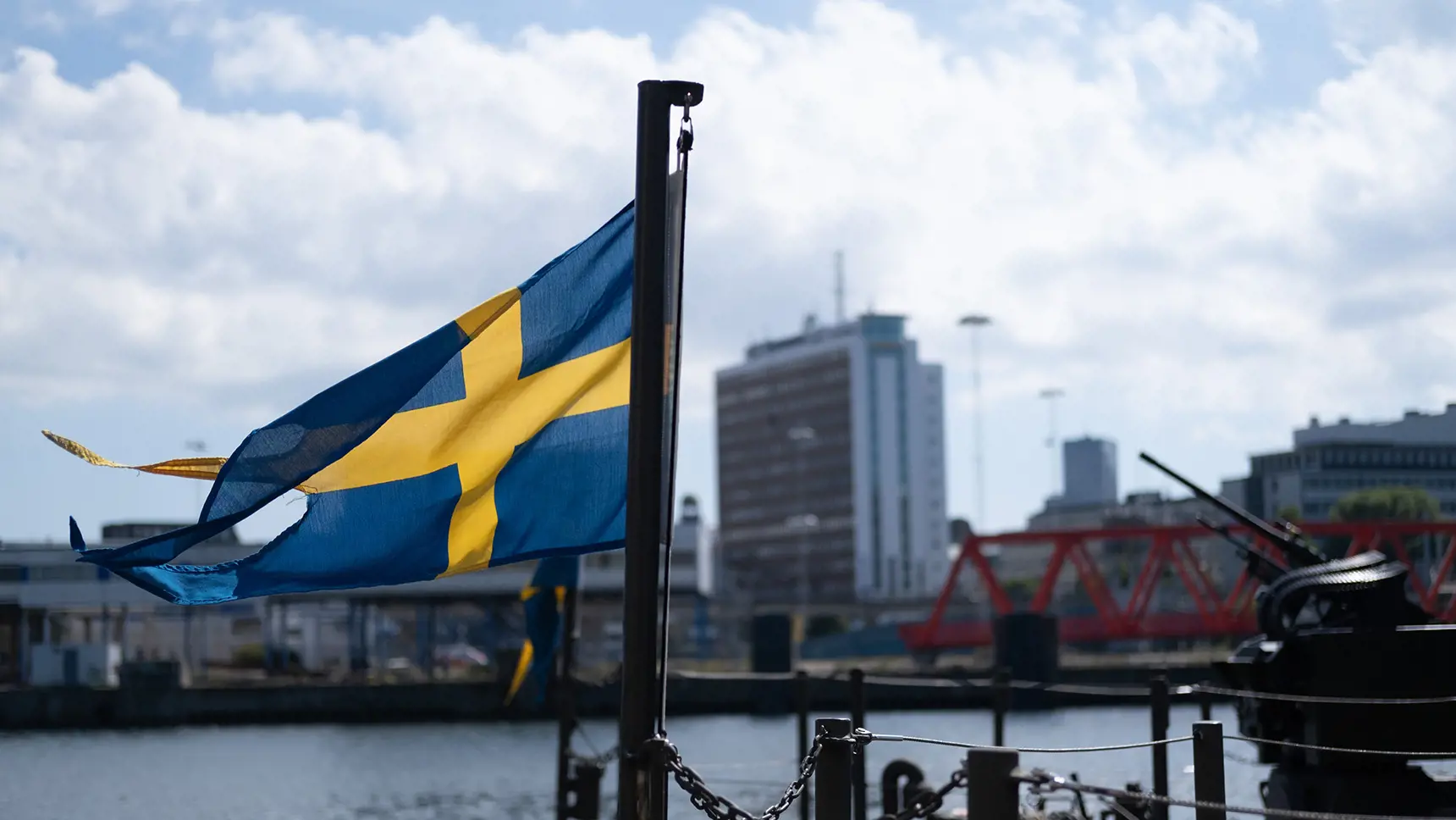 Svensk flagga framför stadsmiljö och himmel.